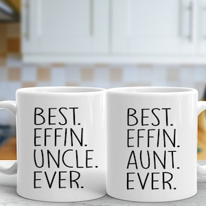 May include: Two white ceramic mugs with black text. The mug on the left says "BEST. EFFIN. UNCLE. EVER." The mug on the right says "BEST. EFFIN. AUNT. EVER."