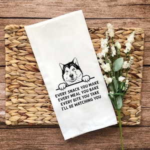 Puede incluir: Una toalla de cocina blanca con una ilustración en blanco y negro de la cabeza de un perro asomándose por la parte superior. El texto dice "EVERY SNACK YOU MAKE EVERY MEAL YOU BAKE EVERY BITE YOU TAKE I'LL BE WATCHING YOU."