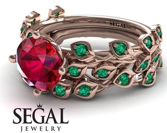 May include: A rose gold engagement ring set with a large red ruby gemstone surrounded by smaller emerald green gemstones. The band features a delicate leaf design. The ring is engraved with the word "SEGAL".