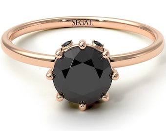 May include: A rose gold ring with a black diamond center stone and smaller black diamonds on the band. The ring is engraved with the word "SEGAL".