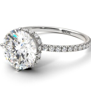 K&ouml;nnte beinhalten: Ein Verlobungsring aus Wei&szlig;gold mit einem gro&szlig;en runden Diamanten in der Mitte und einem Halo aus kleineren Diamanten. Die Ringschiene ist ebenfalls mit kleineren Diamanten besetzt.