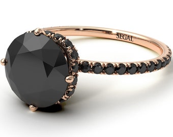 May include: A rose gold engagement ring with a black diamond center stone and a black diamond halo. The band is also set with black diamonds. The ring is engraved with the word "SEGAL".