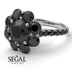 May include: A black diamond engagement ring with a flower-shaped setting. The ring is set in white gold and features a large round black diamond in the center, surrounded by smaller black diamonds. The band is also set with black diamonds.