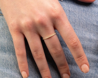 Könnte beinhalten: Ein dünner Goldring mit kleinen Diamanten, die in die Band gefasst sind.