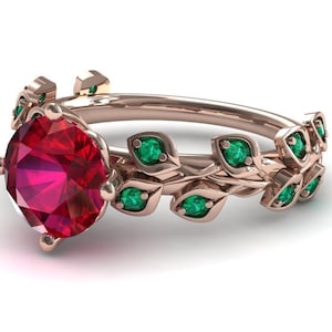 Puede incluir: Un anillo de oro rosa con una gran piedra preciosa de rubí rojo rodeada de un delicado diseño de vid con hojas verde esmeralda.
