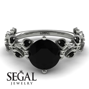 May include: A black diamond engagement ring with a floral design. The ring is set in white gold and features a round black diamond surrounded by smaller black diamonds. The band is adorned with delicate floral details.