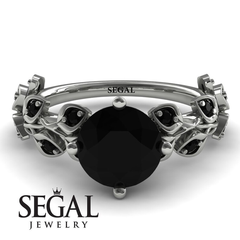 May include: A black diamond engagement ring with a floral design. The ring is set in white gold and features a round black diamond surrounded by smaller black diamonds. The band is adorned with delicate floral details.
