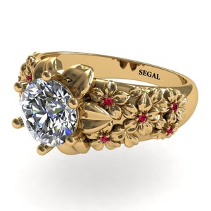 May include: A gold ring with a large round diamond and a floral design. The ring is set with small red gemstones and has the word "SEGAL" engraved on the band.