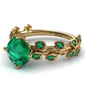 Könnte beinhalten: Ein goldener Ring mit einem großen Smaragd-Edelstein und einem Blattdesign. Der Ring ist mit dem Wort "SEGAL" graviert.
