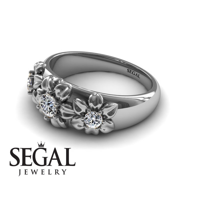 May include: A silver band ring with three flower designs, each with a small diamond in the center. The ring is engraved with the word "SEGAL" on the inside.