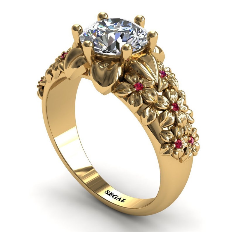 May include: A gold ring with a large, clear center stone and a floral design featuring red gemstones. The ring is engraved with the word "SEGAL".