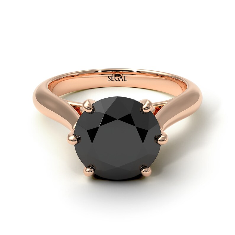May include: A rose gold engagement ring with a black diamond set in a six-prong setting. The ring is engraved with the word "SEGAL".
