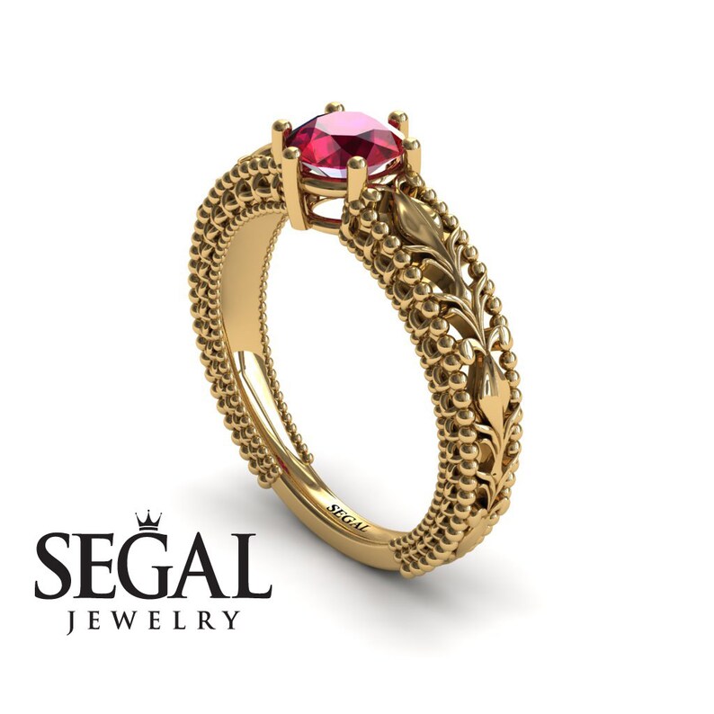May include: A gold engagement ring with a red gemstone and a detailed floral design. The ring is set with a round-cut gemstone and has a beaded band.