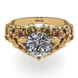 May include: A gold engagement ring with a large round diamond center stone. The band is decorated with a floral design and small red gemstones.