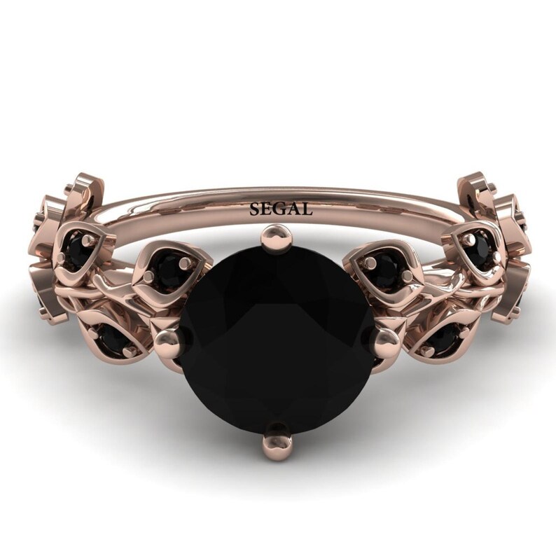 May include: A rose gold ring with a black diamond center stone and black diamond accents on the band. The band is decorated with a leaf design. The ring is engraved with the word "SEGAL".