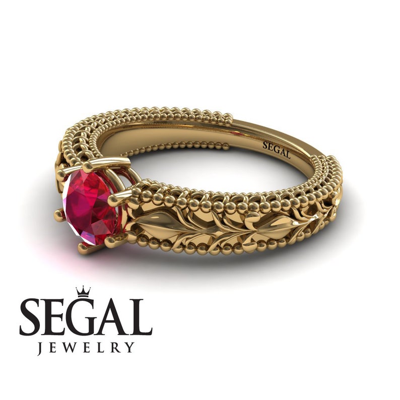 May include: A gold ring with a red ruby gemstone set in a delicate floral design. The band is adorned with a beaded pattern and the inscription "SEGAL" is engraved on the inside of the band.