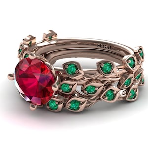 May include: A rose gold engagement ring set with a large ruby gemstone and a band adorned with emerald green leaves. The band is inscribed with the word "SEGAL".