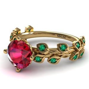 May include: A gold ring with a large red gemstone and a leafy design with emerald green stones. The ring is engraved with the word "SEGAL".