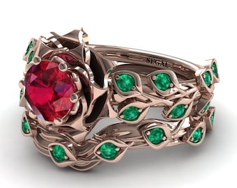 May include: A rose gold engagement ring set with a large red ruby gemstone surrounded by a rose design. The band is adorned with emerald green gemstones set in a leaf design. The band is inscribed with the word "SEGAL".