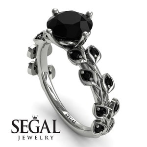 May include: A black diamond engagement ring with a floral design. The ring features a round black diamond center stone and smaller black diamonds set in the band. The band is made of white gold and has a delicate floral design.