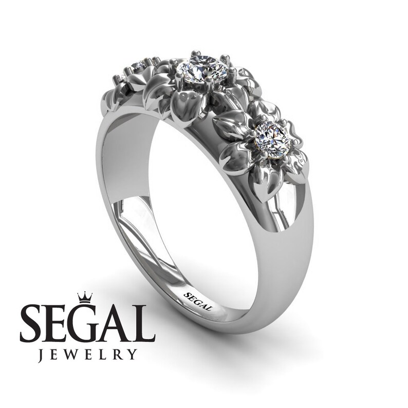 May include: A silver ring with a floral design featuring three diamonds. The ring is engraved with the word "SEGAL".