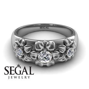 May include: A silver ring with three flower designs, each with a small diamond in the center. The ring is engraved with the word "SEGAL".