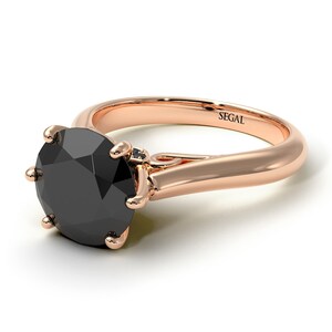 May include: A rose gold engagement ring with a black diamond center stone and a smaller diamond accent. The ring is engraved with the word "SEGAL".