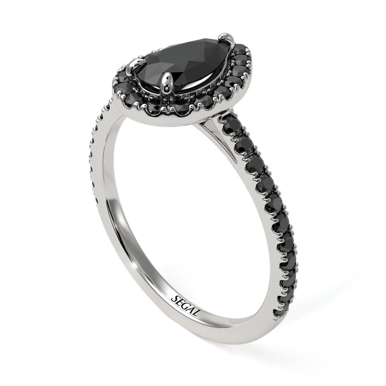 May include: A pear-shaped black diamond engagement ring with a halo of smaller black diamonds. The band is also set with black diamonds. The ring is made of white gold and is engraved with the word "SEGAL".