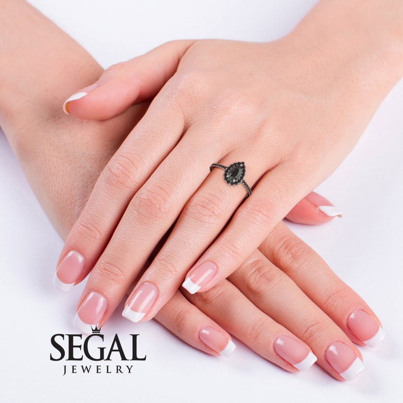 May include: A pear-shaped black diamond engagement ring with a halo of smaller black diamonds set in a black metal band.