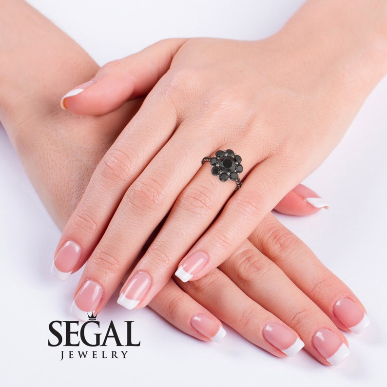 May include: A black diamond engagement ring with a flower design. The ring is set in black metal and features a cluster of round black diamonds.
