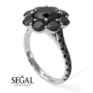 May include: A black diamond engagement ring with a flower-shaped setting. The center stone is surrounded by smaller black diamonds. The band is also set with black diamonds.
