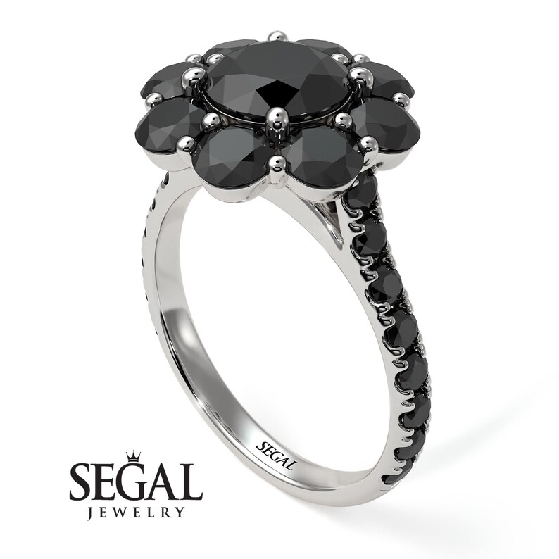 May include: A black diamond engagement ring with a flower-shaped setting. The center stone is surrounded by smaller black diamonds. The band is also set with black diamonds.