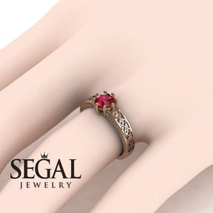 May include: A rose gold engagement ring with a red gemstone and intricate filigree details.