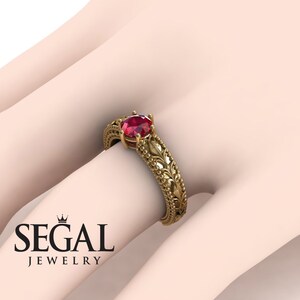 May include: A gold engagement ring with a red gemstone and intricate floral details. The ring is set on a white background.