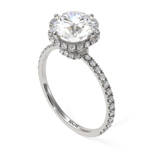 K&ouml;nnte beinhalten: Ein Verlobungsring aus Wei&szlig;gold mit einem gro&szlig;en runden Diamanten in der Mitte, der von einem Heiligenschein aus kleineren Diamanten umgeben ist. Die Ringschiene ist ebenfalls mit kleineren Diamanten besetzt.