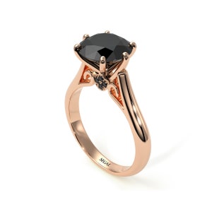 May include: A rose gold engagement ring with a large black diamond center stone and smaller black diamonds on the band. The ring is engraved with the word "SEGAL".