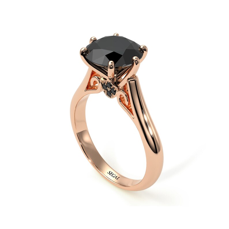 May include: A rose gold engagement ring with a large black diamond center stone and smaller black diamonds on the band. The ring is engraved with the word "SEGAL".