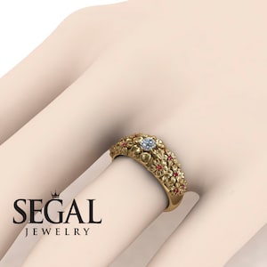 May include: A gold ring with a floral design and a single diamond in the center. The ring is set with small red gemstones around the flowers.