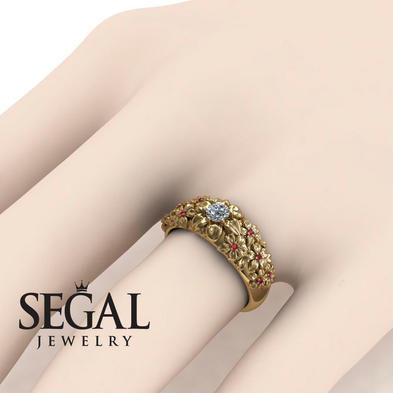 May include: A gold ring with a floral design and a single diamond in the center. The ring is set with small red gemstones around the flowers.