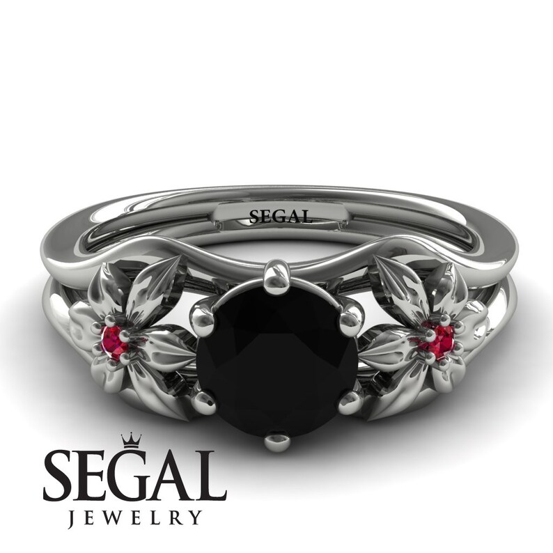 May include: A black diamond engagement ring with two ruby accents set in a floral design. The ring is made of white gold and has the inscription "SEGAL" on the band.