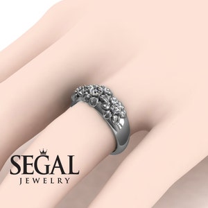 May include: A silver band ring with a floral design featuring three round diamonds. The ring is on a model's finger.