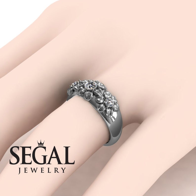 May include: A silver band ring with a floral design featuring three round diamonds. The ring is on a model's finger.