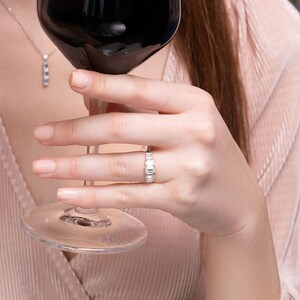 以下が含まれることがあります： 赤いワイングラスを持った女性の手に、小さな透明な長方形の石が並んだ銀の指輪がはめられています。指輪は薬指にはめられています。