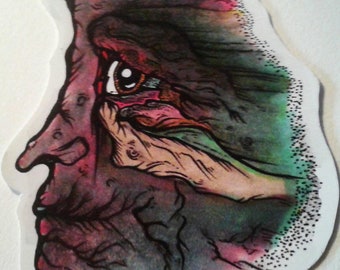 May include: A close-up of a watercolor painting of a face with a single eye. The face is painted in shades of green, blue, and pink, with a textured background.