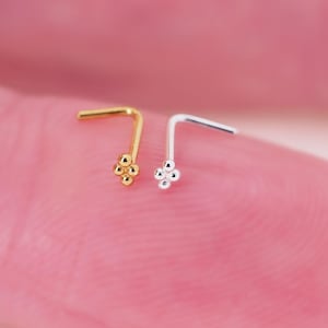 May include: Two nose rings with a flower design. The nose ring on the left is gold and the nose ring on the right is silver.