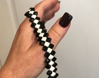 Puede incluir: Un brazalete a cuadros blanco y negro hecho de pequeñas cuentas cuadradas.
