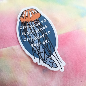 May include: A blue and orange sticker with a jellyfish illustration and the text "It's okay to float along. It's okay to just be."