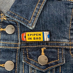 May include: A yellow and blue enamel pin with the text "EPIPEN IN BAG" on a denim jacket.