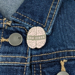May include: A pink brain-shaped enamel pin with the text "the illest" on a denim jacket.