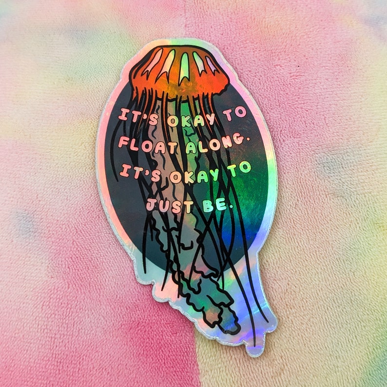 May include: A holographic sticker with a jellyfish illustration and the text "It's okay to float along. It's okay to just be."